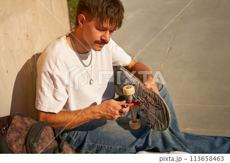View of a man repairing his skateboard in the skate park. Extreme sport concept View of a man repairing his skateboard in the skate park. Extreme sport concept 113658463