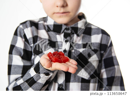 The girl holds red chewable vitamins in the form of bears in her hand. The concept of a multivitamin complex for the health and immunity of children during growth. Vitamin A and B complex, close-up The girl holds red chewable vitamins in the form of bears in her hand. The concept of a multivitamin complex for the health and immunity of children during growth. Vitamin A and B complex, close-up 113658647