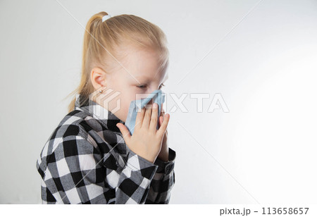 A girl aged seven years old in a checkered shirt blows her nose into a handkerchief on a white background. The concept of nasal congestion due to allergies and acute respiratory infections. Rhinitis A girl aged seven years old in a checkered shirt blows her nose into a handkerchief on a white background. The concept of nasal congestion due to allergies and acute respiratory infections. Rhinitis 113658657