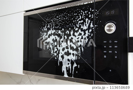 Foam on the microwave screen in the kitchen. The concept of cleaning household kitchen appliances from grease and dirt, close-up 113658689
