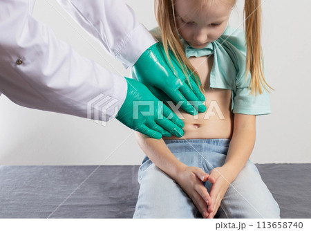 The hands of a therapist doctor palpate the abdomen of a little seven-year-old girl for organ soreness. Inflammation of the abdominal organs, dyspepsia and pain in the intestines, close-up The hands of a therapist doctor palpate the abdomen of a little seven-year-old girl for organ soreness. Inflammation of the abdominal organs, dyspepsia and pain in the intestines, close-up 113658740