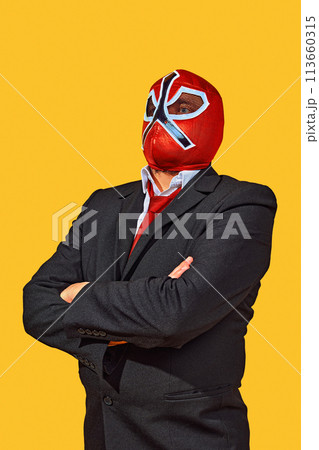 Portrait of confident man in wrestler attire with mask in official attire crossed hand on breast against yellow studio background. 113660315