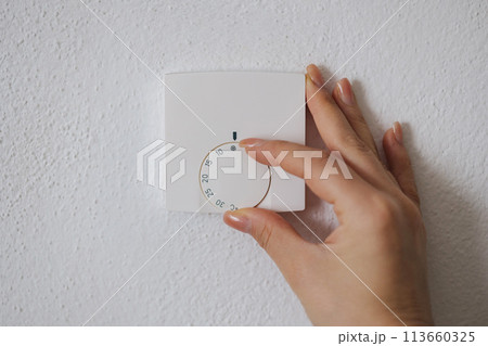 Human hand turns off the heating at home. Central Heating thermostat control dial adjustment 113660325