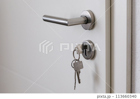 Closed door with keys in the lock. White door and metal handle 113660340