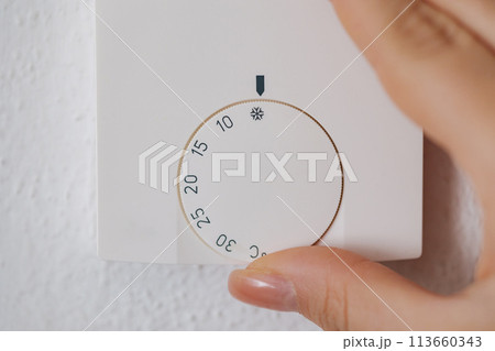 Close-up of human hand turns off the heating at home. Central Heating thermostat control dial adjustment. Woman turning down heating thermostat to save money. 113660343