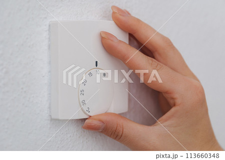Hand turns down the temperature to 10 degrees Celsius on an electronic thermostat. Symbol for saving energy. An empty house during the holidays 113660348