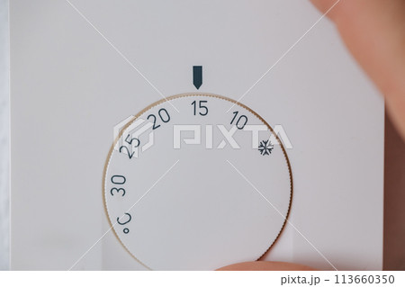 Close-up of hand turns down the temperature to 15 degrees Celsius on an electronic thermostat. Saving energy and money. Cold spring Close-up of hand turns down the temperature to 15 degrees Celsius on an electronic thermostat. Saving energy and money. Cold spring 113660350