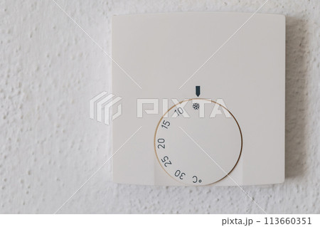 Thermostat with the external and target temperatures indicated. Rotary dial to control and adjust. White wall and white frame 113660351