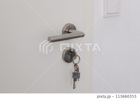 Closed door with keys in the lock. White door and metal handle 113660353