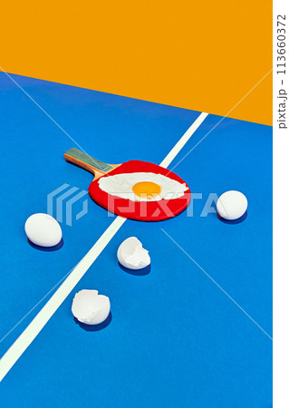 Tennis racquet with fried egg sitting on tennis table on it as on frying pan on kitchen against yellow studio background. Tennis racquet with fried egg sitting on tennis table on it as on frying pan on kitchen against yellow studio background. 113660372