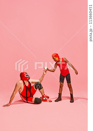 Boy in superhero dressed red costume gave glass of milk to his older, bigger partner against pink studio background. Boy in superhero dressed red costume gave glass of milk to his older, bigger partner against pink studio background. 113660451