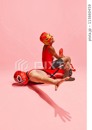 Two athletes, man and boy in red outfit with mask playing, fighting against pink studio background. Have fun together Two athletes, man and boy in red outfit with mask playing, fighting against pink studio background. Have fun together 113660459