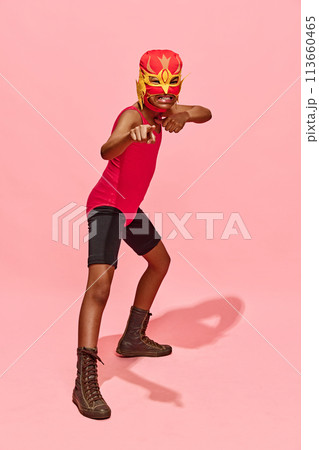 One angry preteen boy stands in attack pose in superhero costume and mask against pink studio background. One angry preteen boy stands in attack pose in superhero costume and mask against pink studio background. 113660465