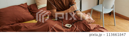 Web banner with sick man sitting on bed and measuring blood pressure 113661847