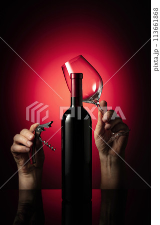 Unopened bottle of red wine and hands with corkscrew and wine glass. Unopened bottle of red wine and hands with corkscrew and wine glass. 113661868