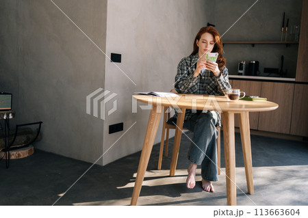 Wide remote shot of sad young unemployment woman counting remaining money sitting at home table due to economic financial crisis. Empty wallet. Bankrupt, poverty, tax, money concept. 113663604
