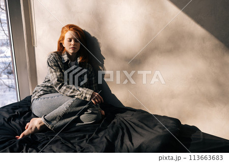 Portrait of depressed young woman sitting on sunny day on floor by window alone, having melancholic mood, troubled with loneliness, upset about solitude mental problem, regret bad mistake concept. Portrait of depressed young woman sitting on sunny day on floor by window alone, having melancholic mood, troubled with loneliness, upset about solitude mental problem, regret bad mistake concept. 113663683