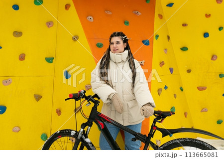 Woman Standing Next to Bike in Front of Climbing Wall 113665081