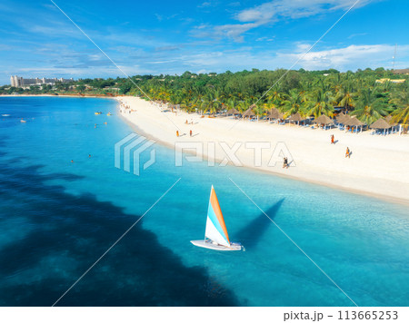 Aerial view of the sailboat on blue sea with white sandy beach Aerial view of the sailboat on blue sea with white sandy beach 113665253