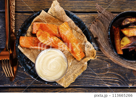 pieces of battered fish on a plate with baked potato on a wooden table with space pieces of battered fish on a plate with baked potato on a wooden table with space 113665266