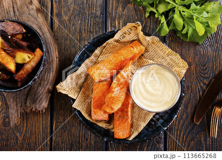 pieces of battered fish on a plate with baked potato on a wooden table with space pieces of battered fish on a plate with baked potato on a wooden table with space 113665268