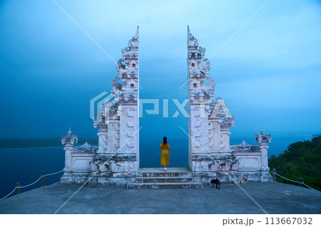 A woman in a yellow dress stands at a famous Balinese traditional gate on the island of Nusa Penida. 113667032