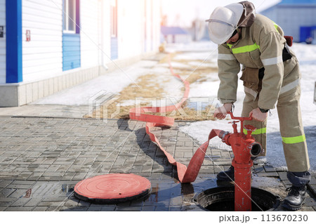 Image of a firefighter connecting a red fire hose to a hydrant for emergency water supply Image of a firefighter connecting a red fire hose to a hydrant for emergency water supply 113670230