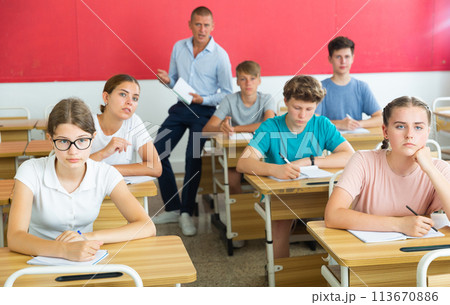 Teenage students are sitting at their desks in classroom. In background the teacher 113670886
