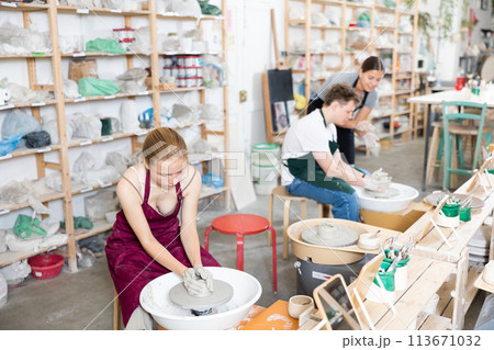 Young woman teacher helps teenagers boy and girl to make product on potter's wheel 113671032