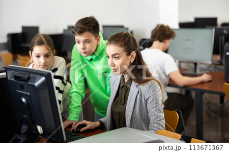 Teacher helping girl and boy to solve computer problem 113671367