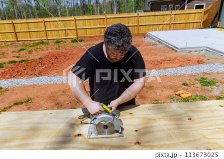 Carpenter trims plywood boards with handsaw 113673025