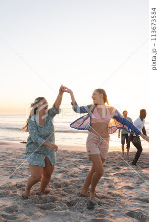 Two young Caucasian women enjoy a playful dance on the beach at sunset Two young Caucasian women enjoy a playful dance on the beach at sunset 113673584