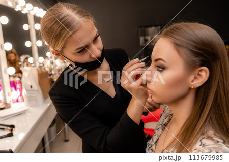 Make-up artist paints eyebrow pencil to beautiful brunette in be 113679985
