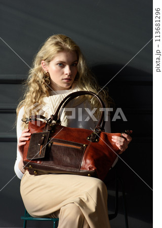 beautiful curly blond hair woman posing with a brown shopper bag near gray wall beautiful curly blond hair woman posing with a brown shopper bag near gray wall 113681296
