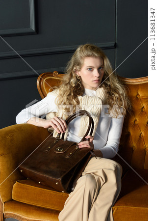 beautiful curly blond hair woman posing with a small shopper brown bag in a vintage chair beautiful curly blond hair woman posing with a small shopper brown bag in a vintage chair 113681347