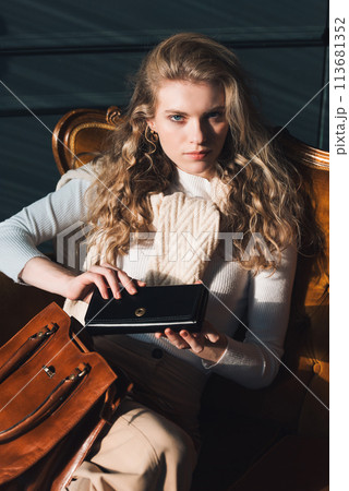 beautiful curly blond hair woman posing with a wallet and small shopper brown bag in a vintage chair beautiful curly blond hair woman posing with a wallet and small shopper brown bag in a vintage chair 113681352