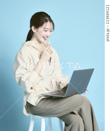 青背景で撮影したPCで作業をしている若い女性 青背景で撮影したPCで作業をしている若い女性 113684121