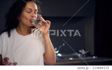 Close-up portrait of a pretty young woman drinking water in the morning, starting her day with a glass of refreshing water 113684172