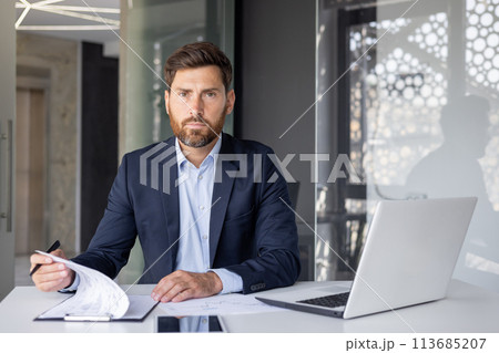 Portrait of a young businessman, executive director and newbie of the company sitting in the office at the desk and working with documents. 113685207