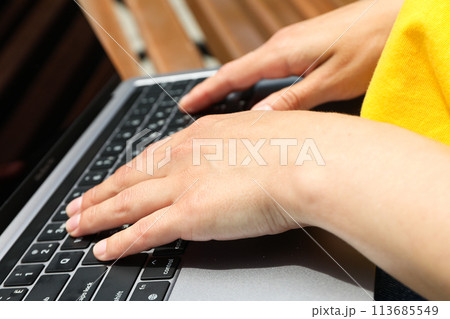 The girl works on a laptop while sitting on a bench 113685549