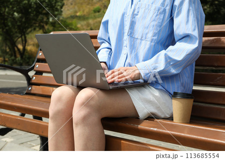 The girl works on a laptop while sitting on a bench 113685554