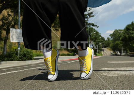 Stylish yellow sneakers on women's legs on the asphalt 113685575