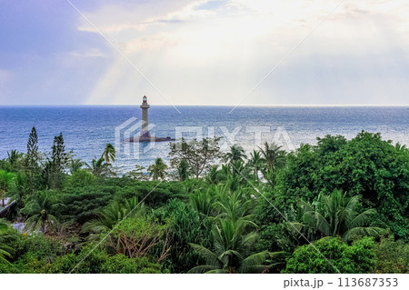 View of a lighthouse in the sea near a rocky shore with palm trees. End of the World Park, Sanya. 113687353