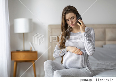 Worried pregnant woman talking on phone at home 113687517