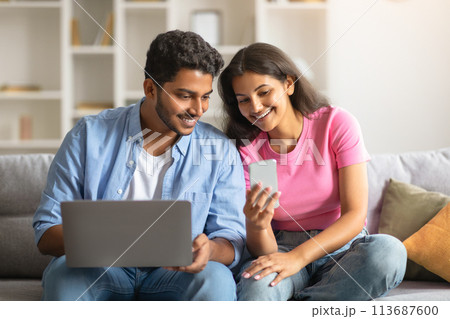 Cheerful indian couple using laptop and smartphone on sofa Cheerful indian couple using laptop and smartphone on sofa 113687600