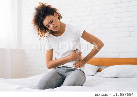 African-american girl suffering from abdominal pain on bed African-american girl suffering from abdominal pain on bed 113687684