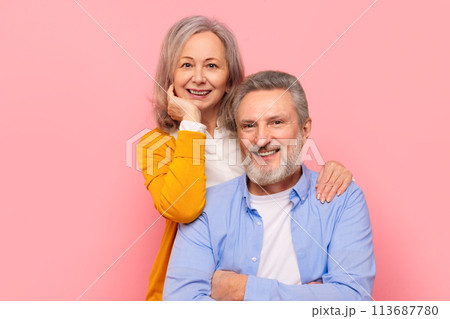 Smiling senior couple hugging posing for portrait against pink backdrop Smiling senior couple hugging posing for portrait against pink backdrop 113687780