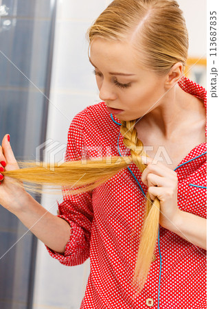 Blonde woman looking at her hair ends 113687835