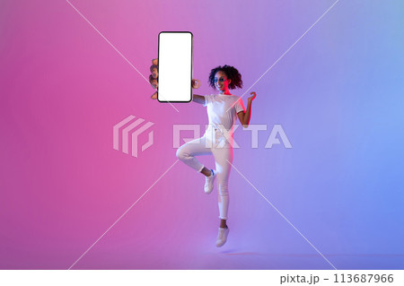 Energetic black woman jumping with blank smartphone screen on neon background 113687966