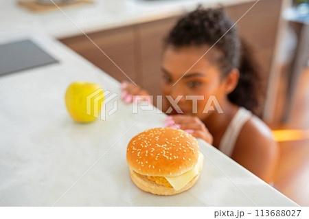 woman battles temptation at kitchen choosing between apple and cheeseburger 113688027